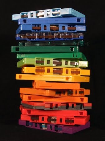 A stack of plastic cassette tapes without cases, stacked by color to resenble a rainbow