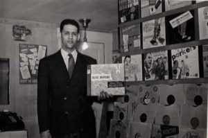 Harold Kelley holds "Blue Danube," a 78 record. Single 78s are visible on the rack below. Behind him is the store's soundproof listening booth. Circa 1949.