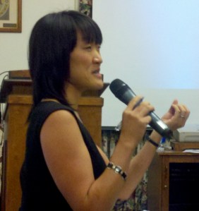 A woman holds a microphone with her left hand and gestures with the right. Nina Sun Eidsheim, Image by Renate Ferro