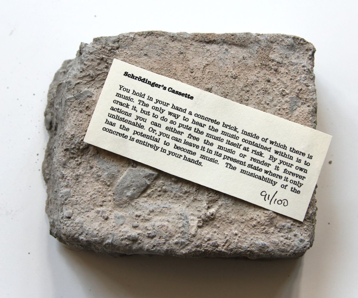 image of cement encased-tape with the tag: Schrödinger's Cassette: You hold in your hand a concrete brick, inside of which there is music. The onlu way to hesr the music contained within is to crack it, but to do so puts the music itself at risk. By your own actions you can either free the music or render it forever unlistenable. Or, you can leave it in its oresent state where it only has the potential to become music. The musicability of the concrete is entirely in your hands" 91/100