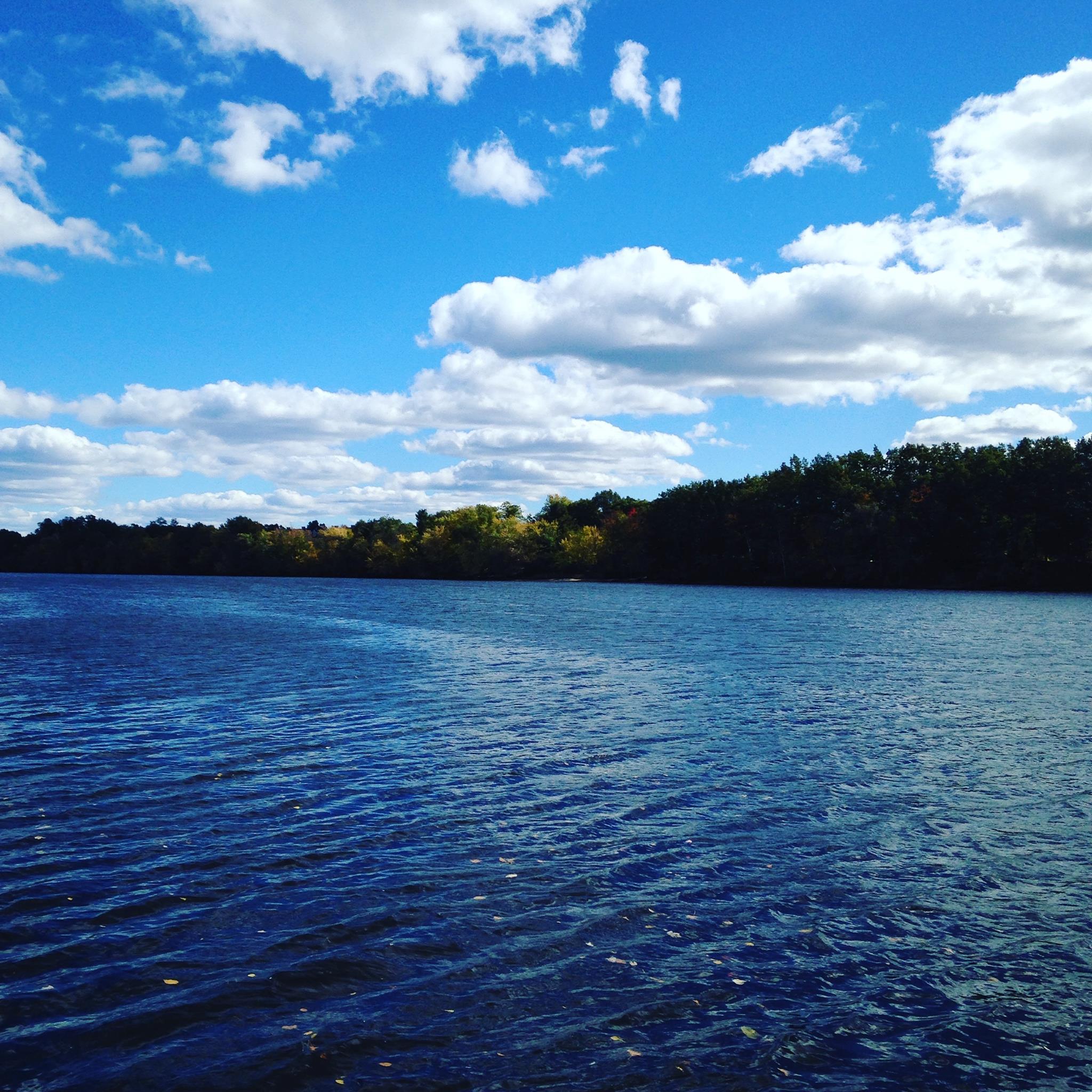 The Merrimack River is a rich, dark, blue and swiftly flowing according to the ripples in this image. There is a light blue sky with white puffy clouds visible in the distance as well as a bank with green trees. Lowell Massachusetts, USA. All images by author.